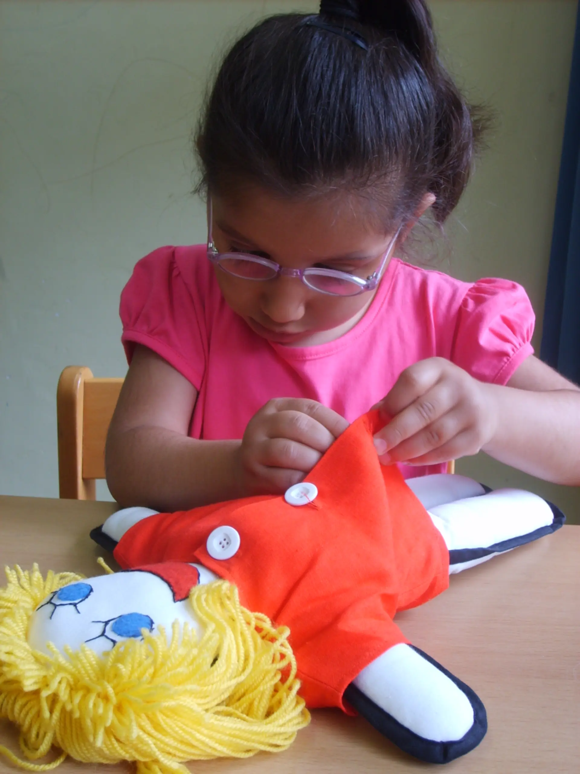 Mädchen knöpft ihrer Puppe das Kleid zu