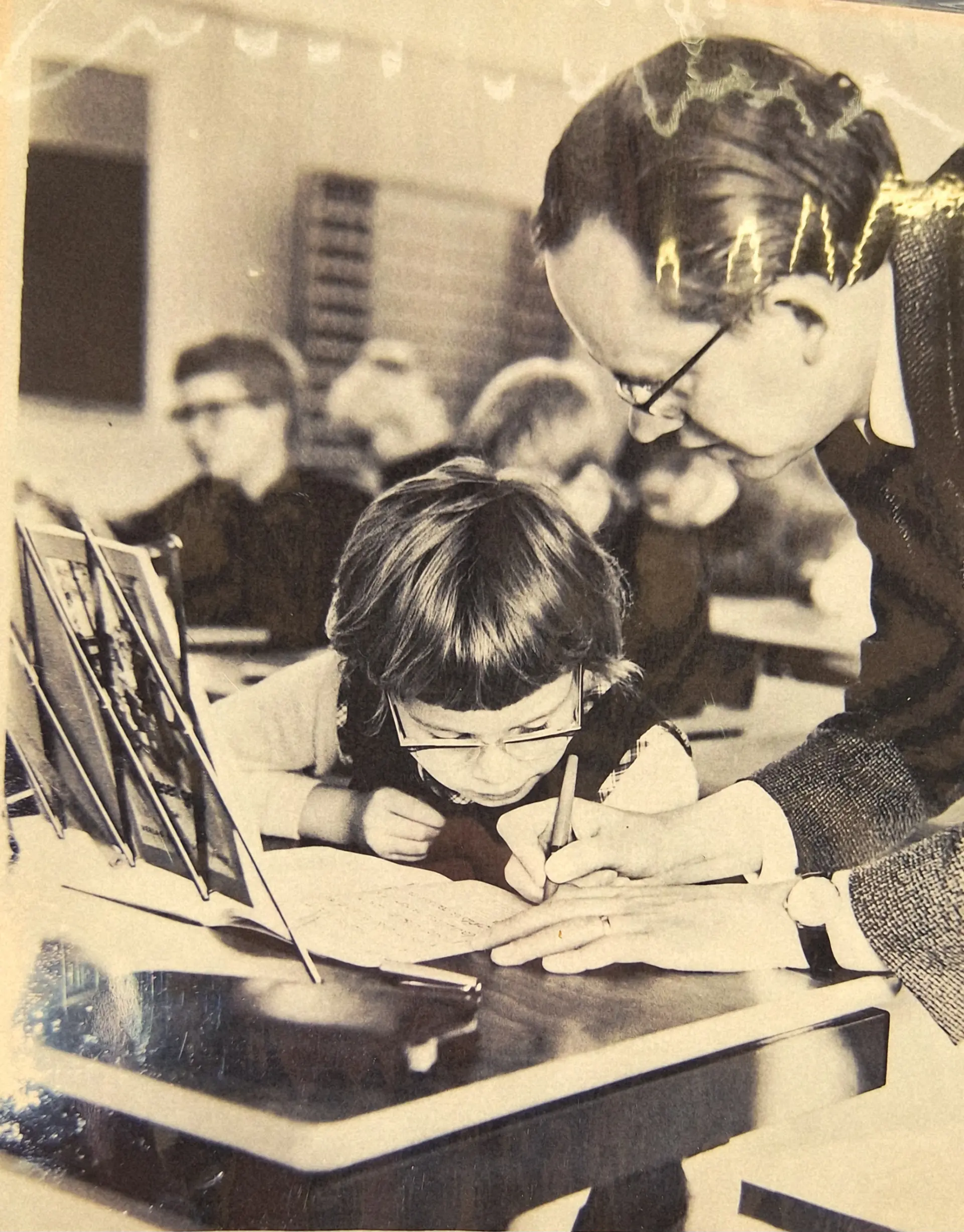 Lehrkraft hilft sehbeeinträchtigtem Kind beim Schreiben