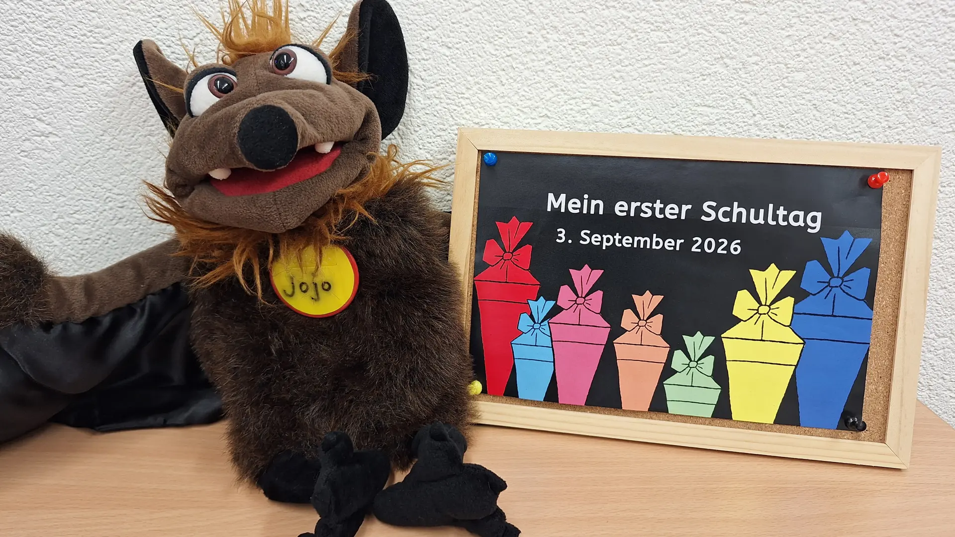 Das Maskottchen Jojo der Fledermausklasse neben dem Einschulungsschild